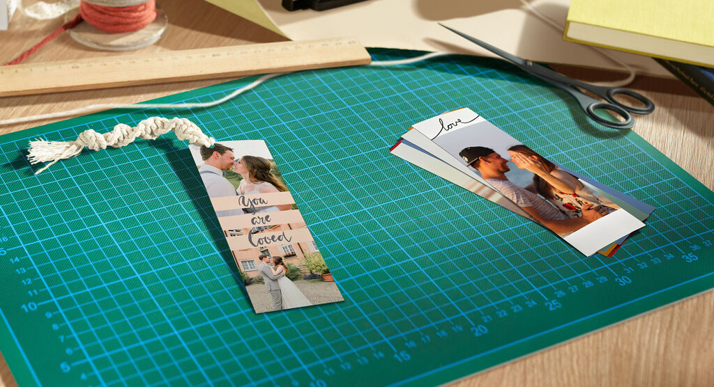 Su un tavolo da lavoro si vedono due segnalibri personalizzati con foto di un matrimonio.