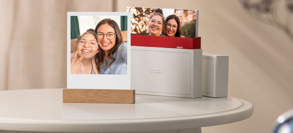 Due persone tengono in mano una foto mentre un fotolibro CEWE è su un tavolo