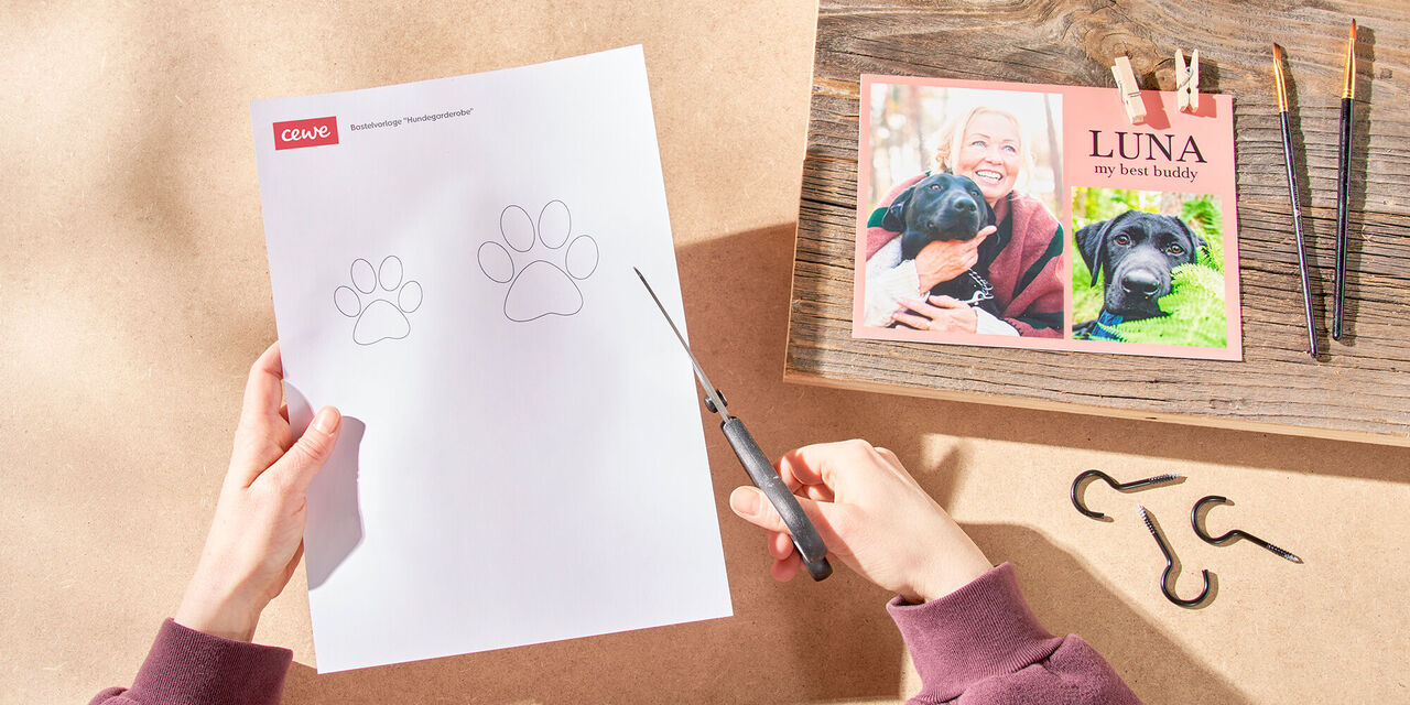 Persona che taglia impronte di zampe da un foglio di carta su un tavolo con fotolibro CEWE.