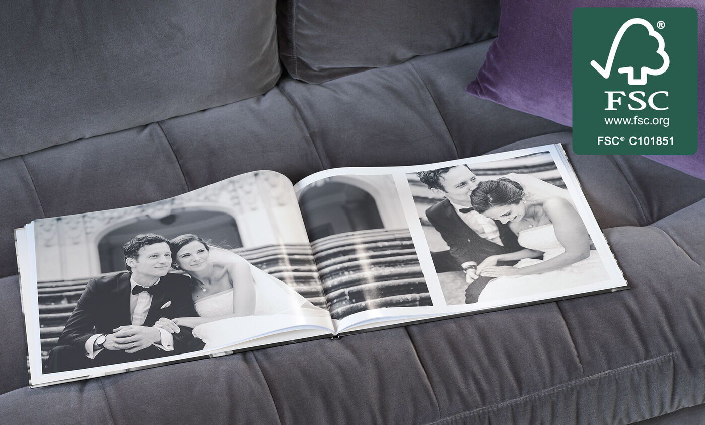 Un CEWE FOTOBOOK aperto su un divano grigio con una romantica doppia pagina di matrimonio in bianco e nero.