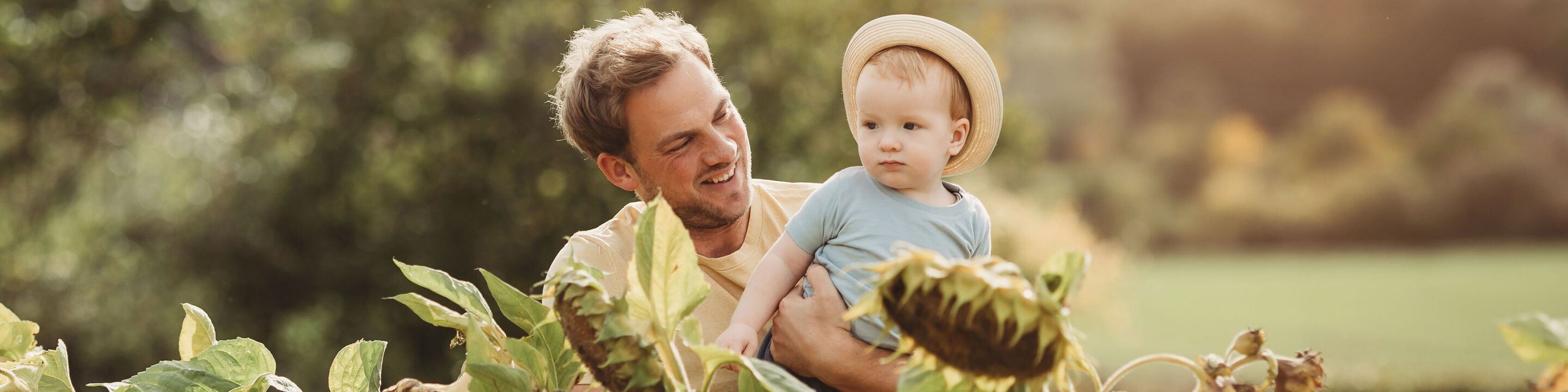 Un padre felice tiene il bambino in un prato di girasoli sotto il sole.