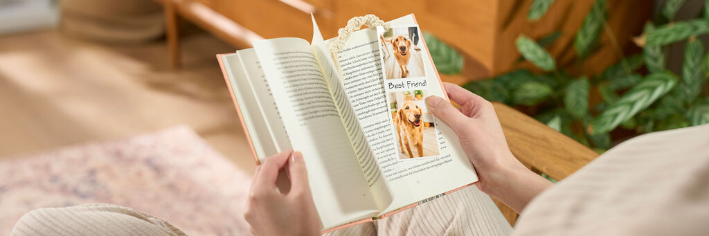 Una persona è seduta e tiene in mano un libro aperto in cui si vede un segnalibro personalizzato creato fai da te con foto istantanee di un cane.