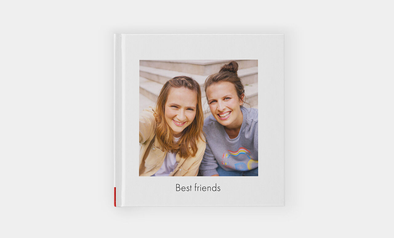 Due amiche sorridenti tengono un fotoalbum intitolato 'Best Friends'.